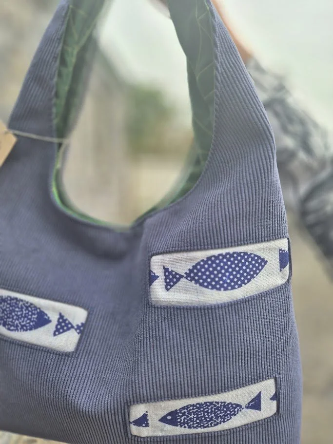 A blue fabric bag with patches of blue fish illustrations on a light background.