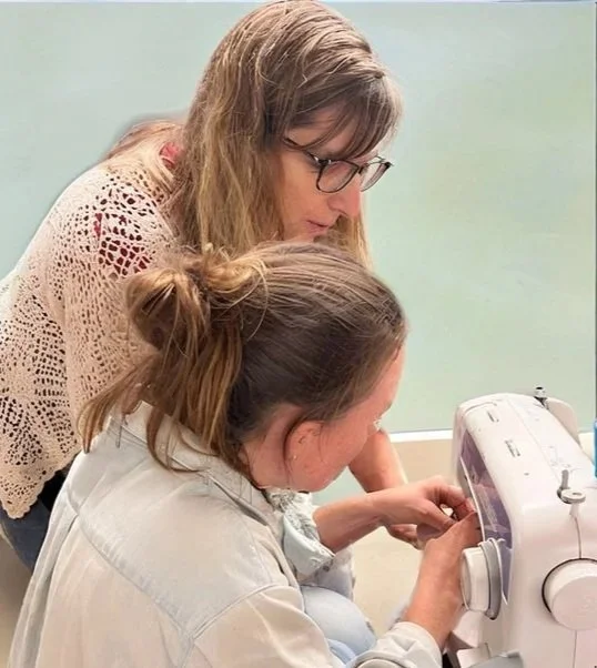 Two women working together on a sewing machine in a classroom setting.