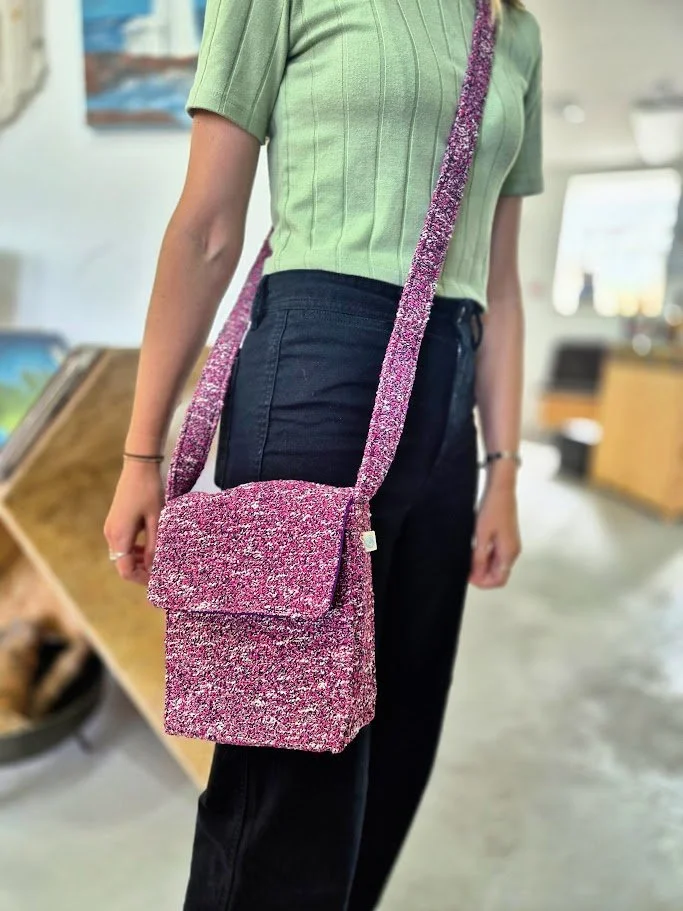 Person wearing a green top and black pants, carrying a sparkly pink handbag with a matching strap, in a store setting.