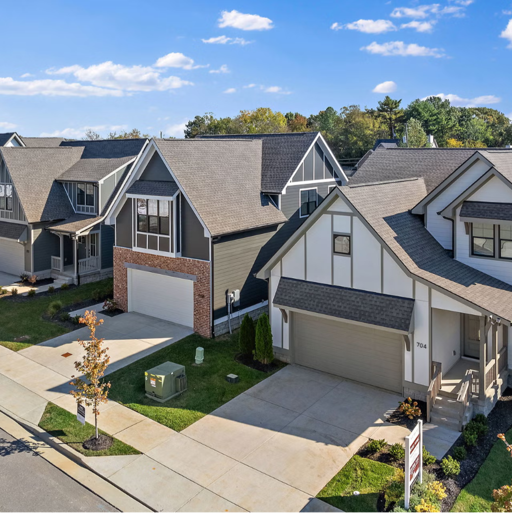 A neighborhood of modern suburban houses with gray and white exteriors and attached garages, under a blue sky with scattered clouds.