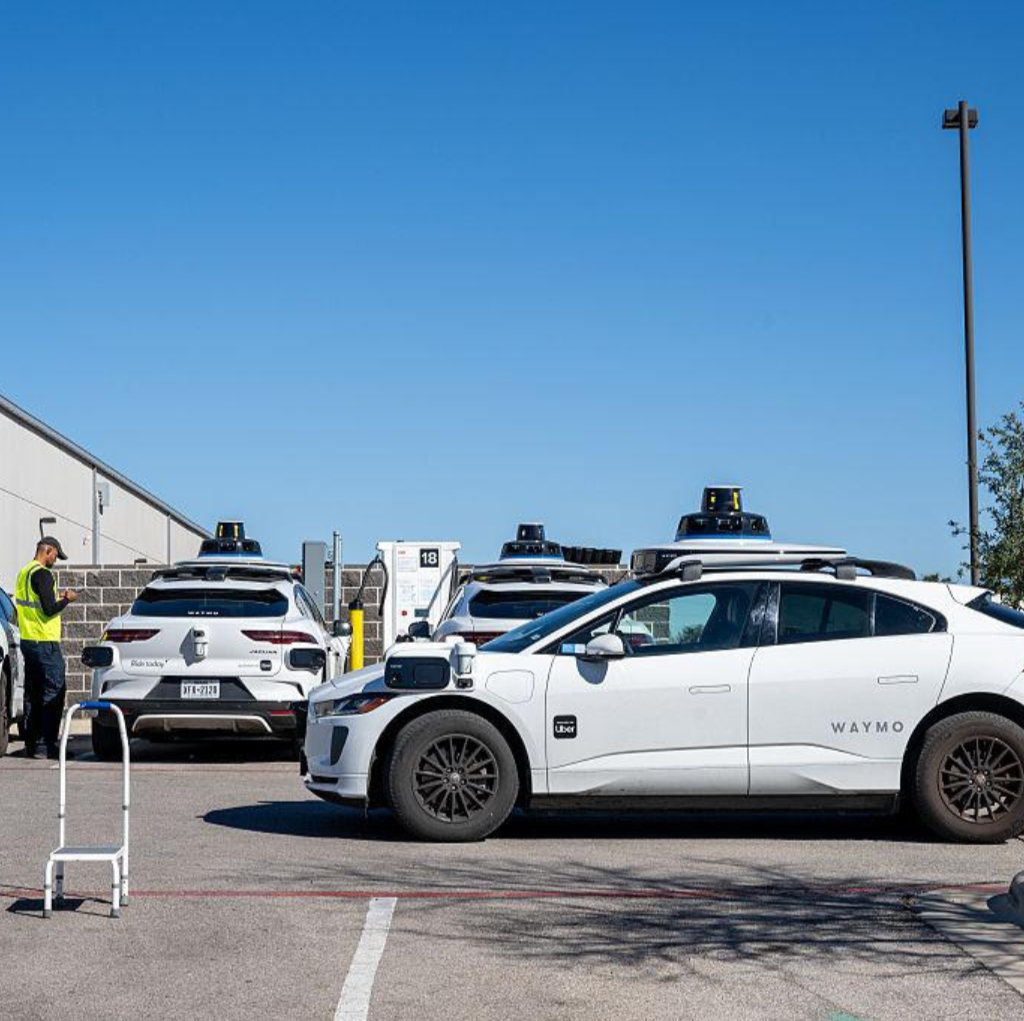Several police cars and a Uber Waymo self-driving car parked in a lot under a clear blue sky.