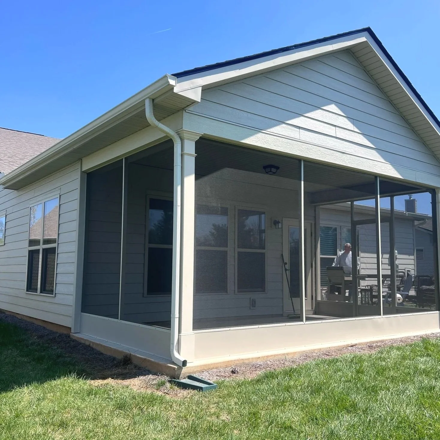 Backyard of a house with a screened-in porch, a man standing inside, and sunny weather.