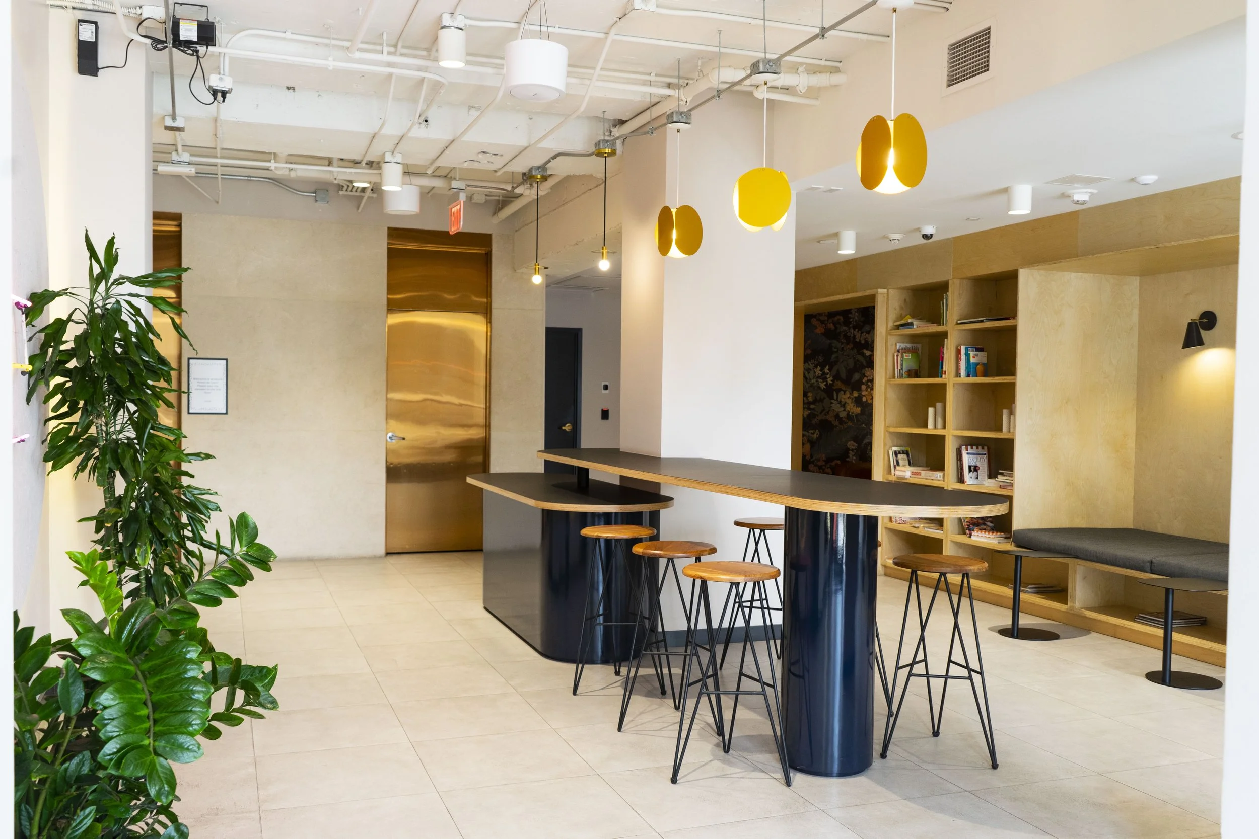 Bright living room with large beige sectional sofa, coffee table with plants, flat-screen TV on white wall, sliding glass doors with outdoor view, and tropical plants outside.