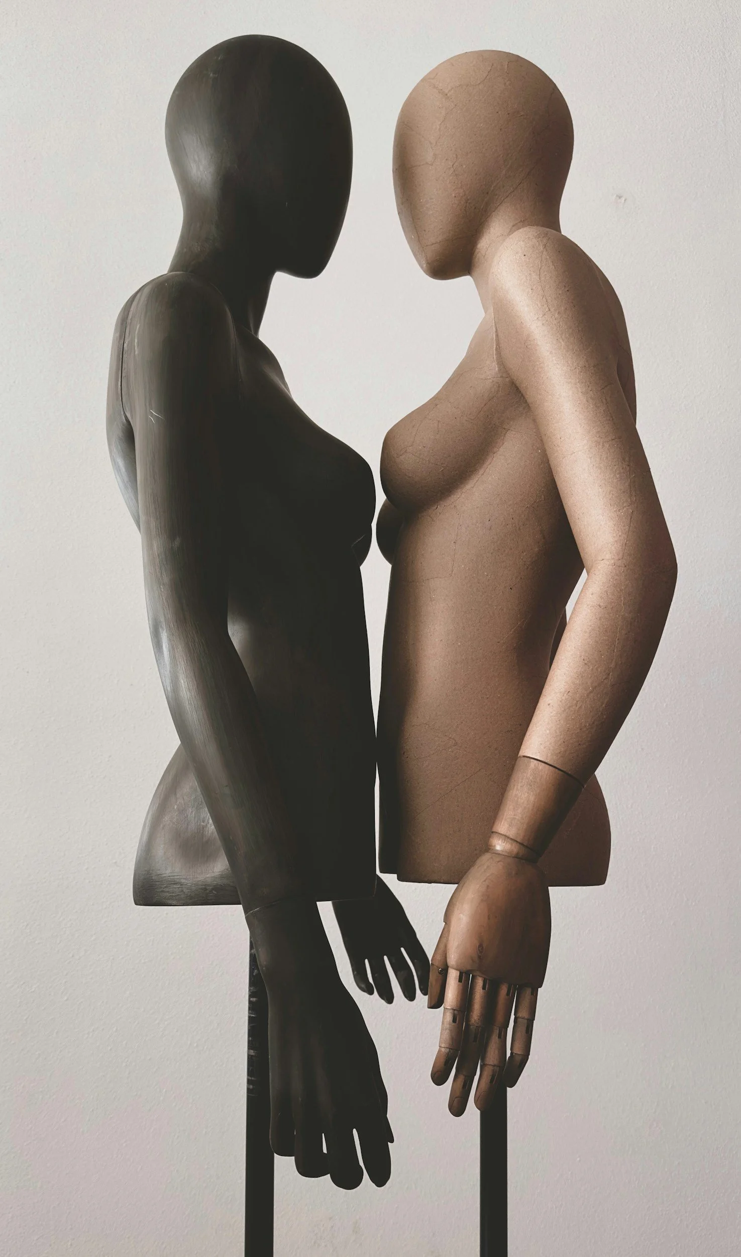 Two mannequin sculptures, one black and one tan, standing face-to-face with hands touching.