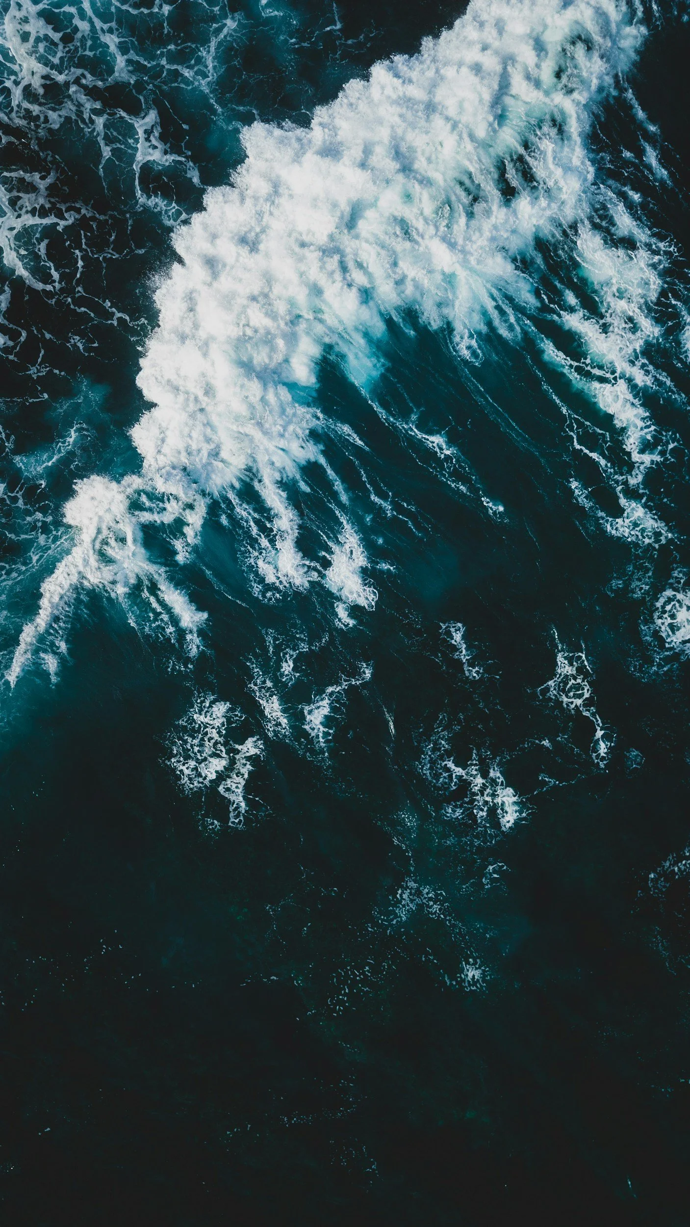 Aerial view of ocean waves with white foam and dark blue water.