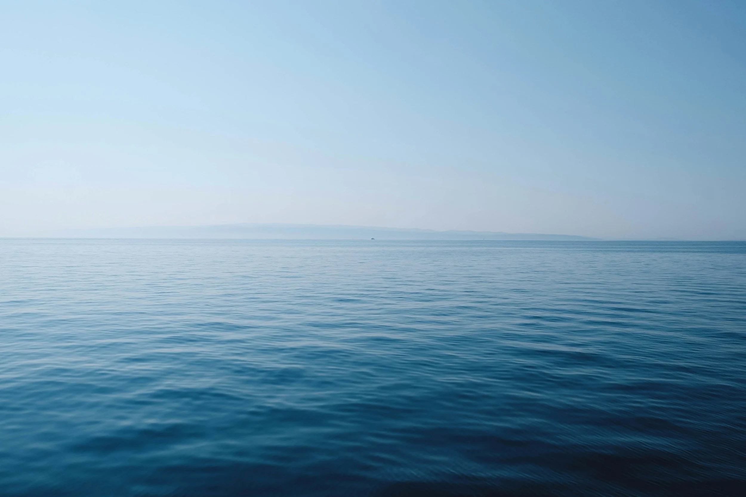 A vast expanse of calm ocean water with a light blue sky above.