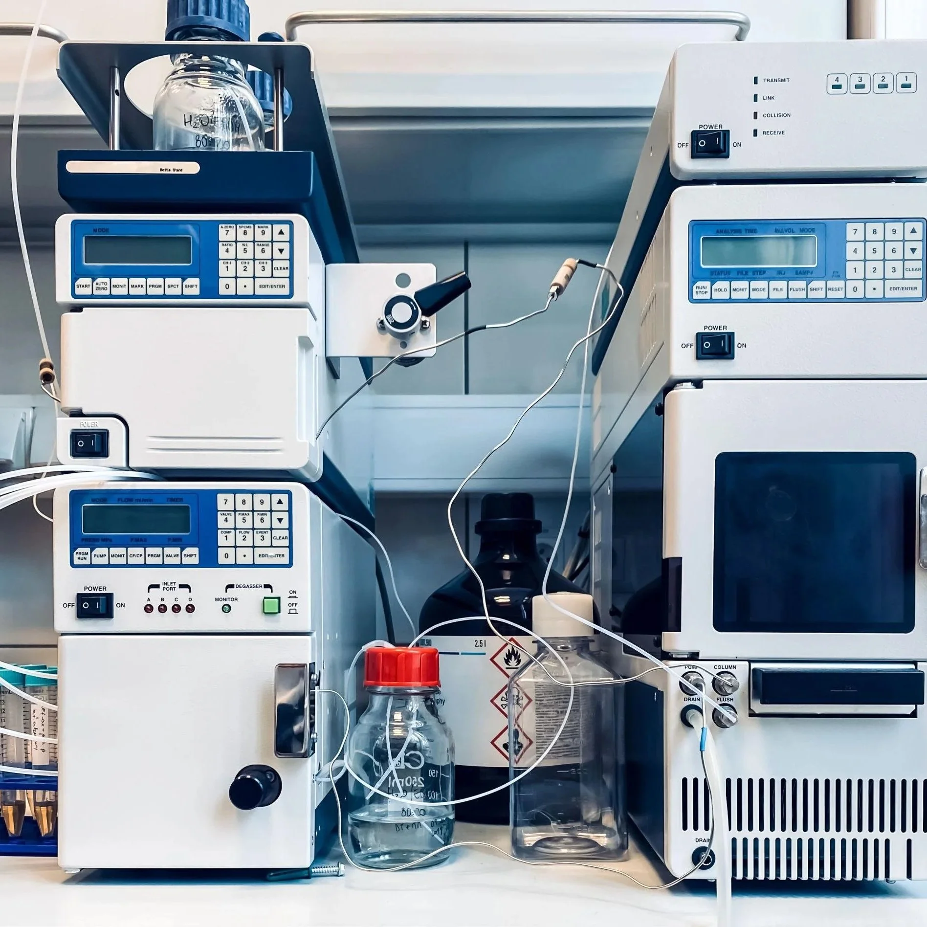 Laboratory setup with medical or scientific equipment, including a glass container connected with tubing, and two white machines with control panels, buttons, and display screens, placed on a white surface.