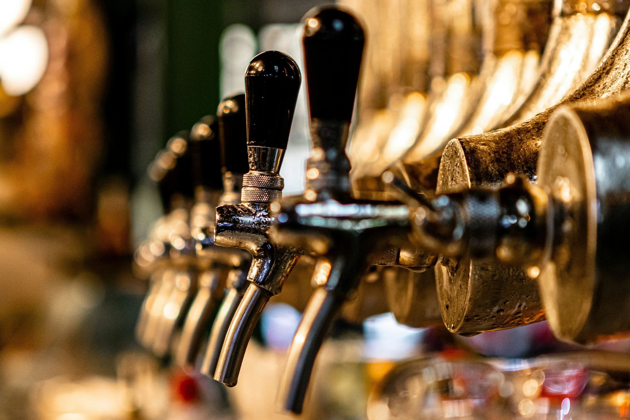 Close-up of beer tap handles at a bar, with a blurry background.