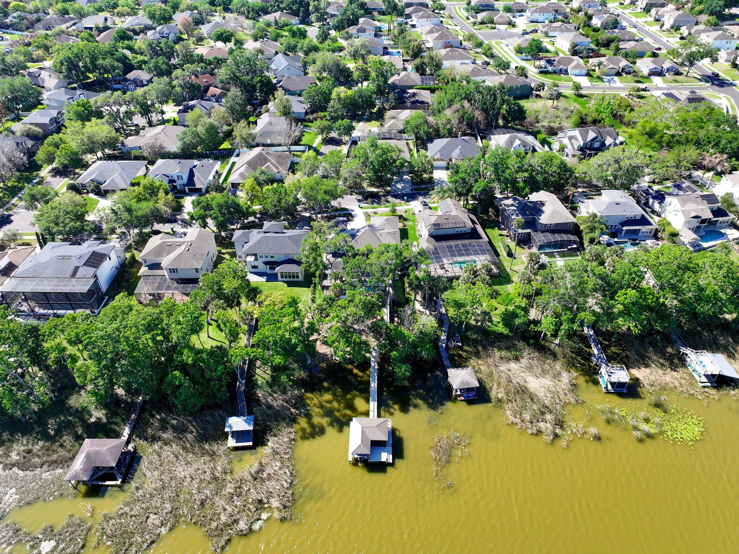 An aerial view of a suburban neighborhood with houses, trees, and a waterway with several boat docks.