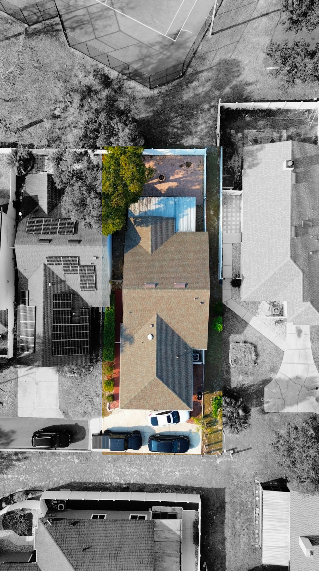 Color photo of a single-story house with a brown roof, trees in the yard, and three parked cars in the driveway, with neighboring houses and streets visible.