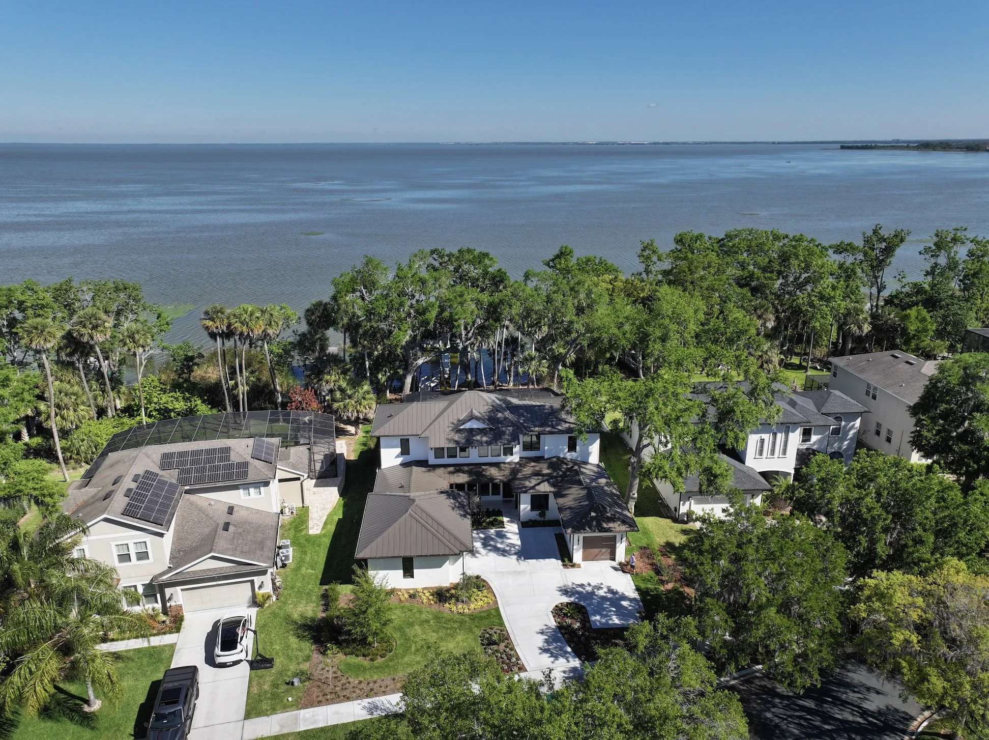 Residential neighborhood with houses, trees, and a large body of water in the background under a clear blue sky.