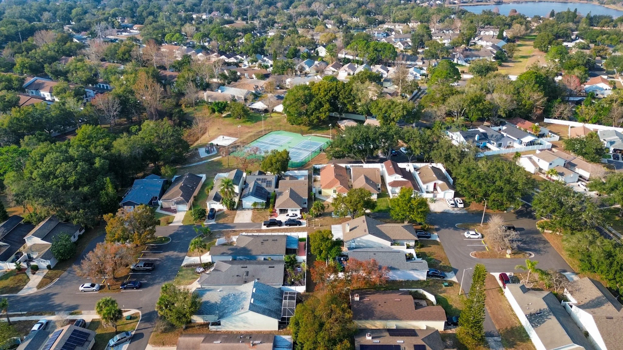 Aerial view of a suburban neighborhood with numerous houses, trees, and a recreational area with tennis courts.
