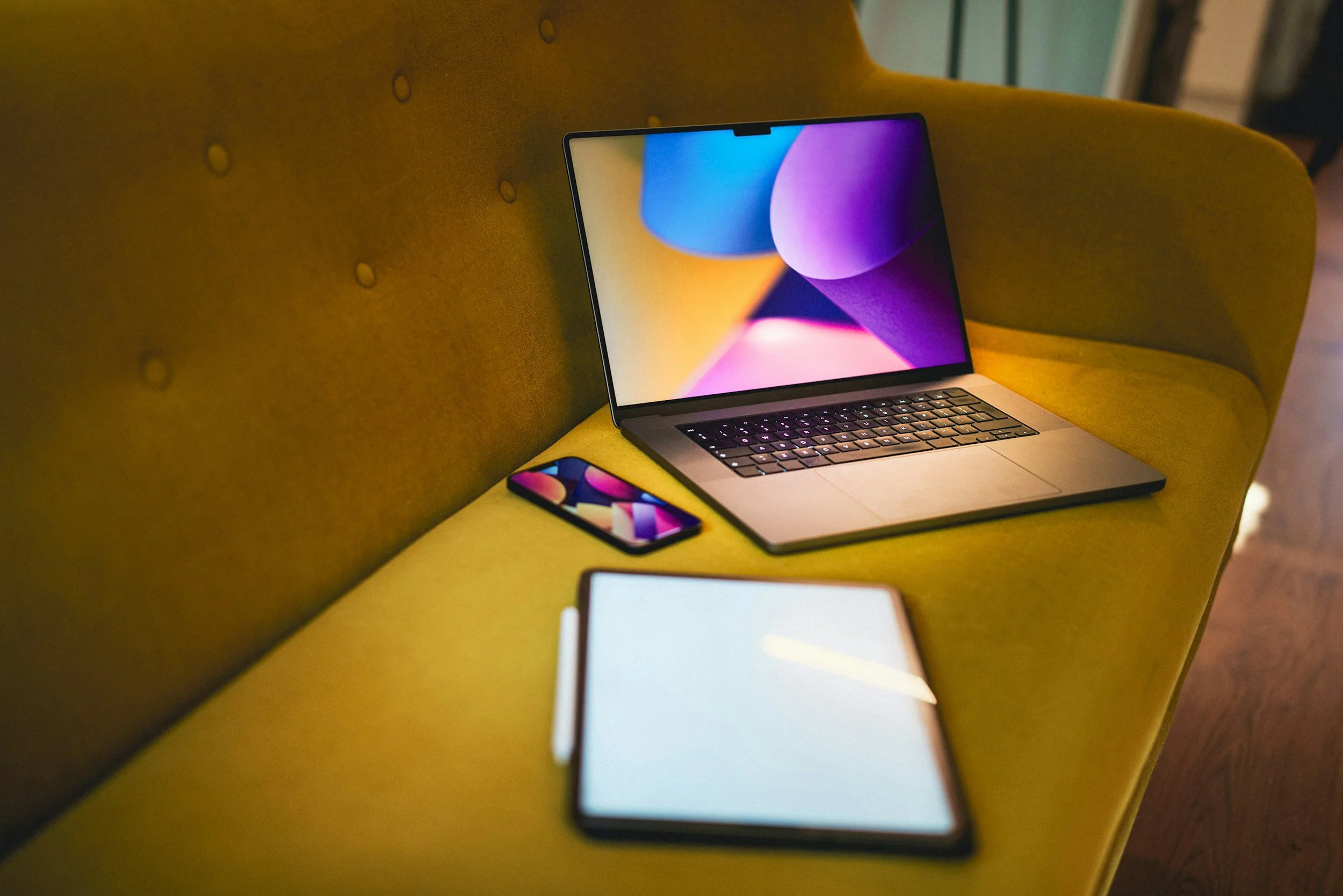 Laptop, smartphone, tablet, and notebook on a yellow couch.