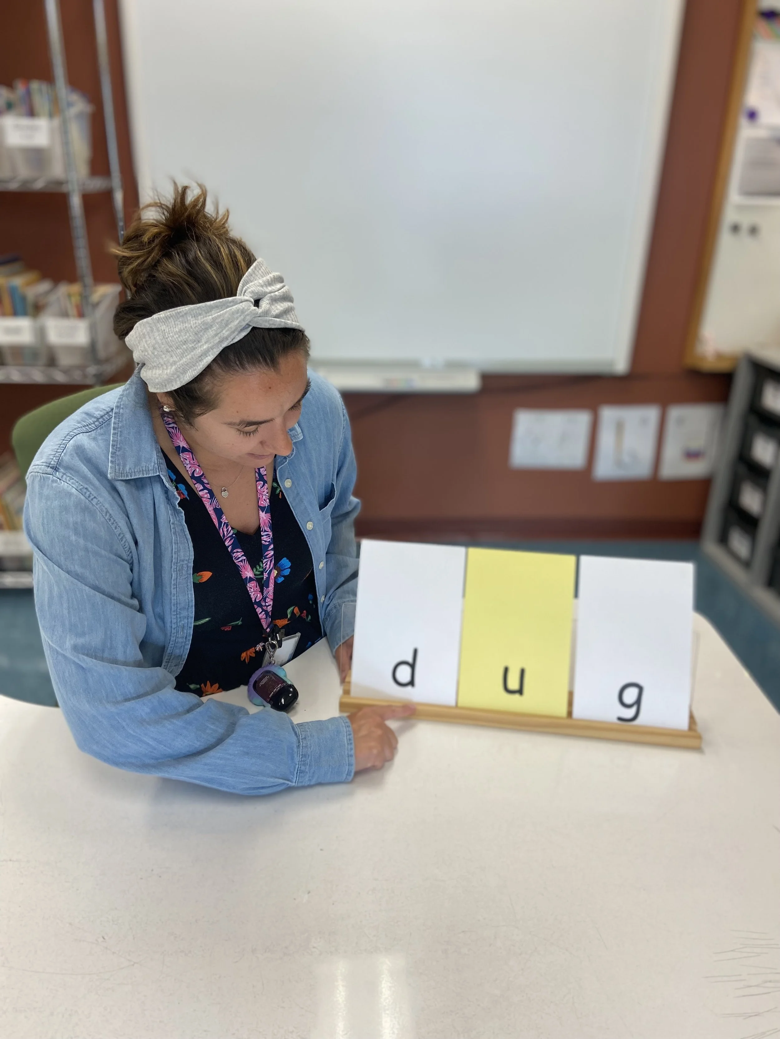 A woman pointing at a flip chart with the letters D, U, G on it, in a classroom setting.