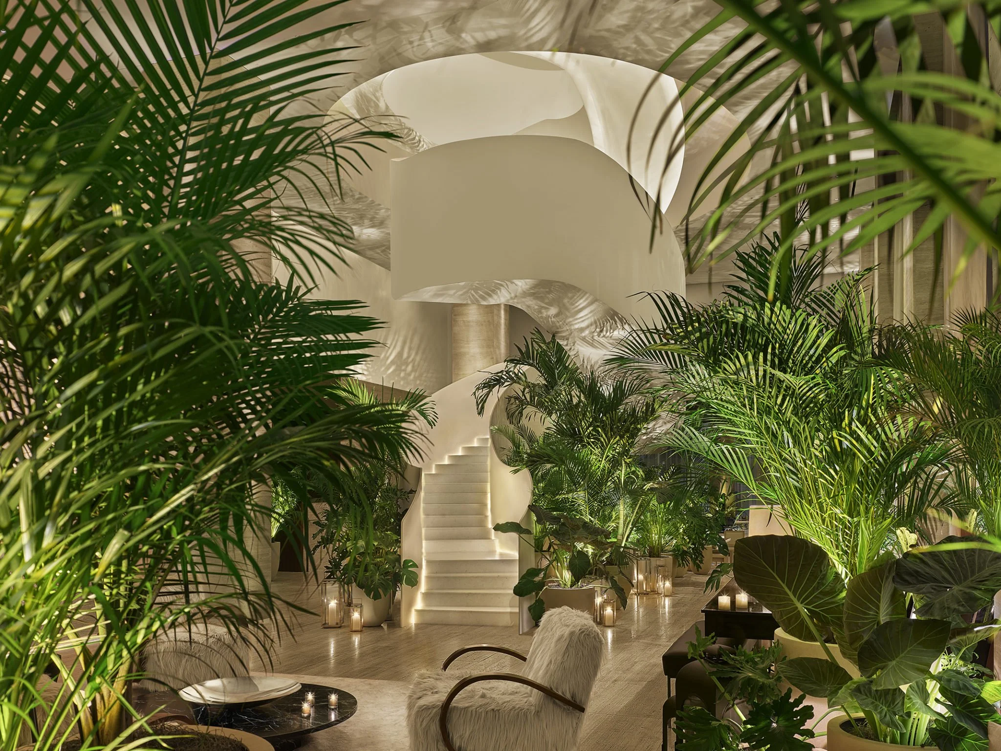 Luxury interior with lush green tropical plants, a white staircase, and ambient candle lighting.