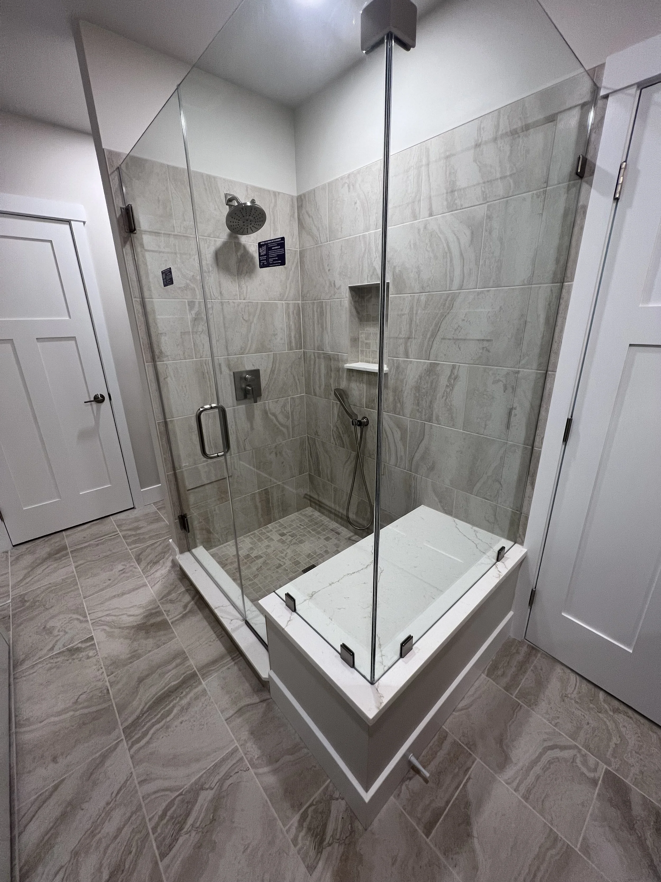 Modern walk-in shower with beige marble tiles, glass walls, and a built-in niche and bench.