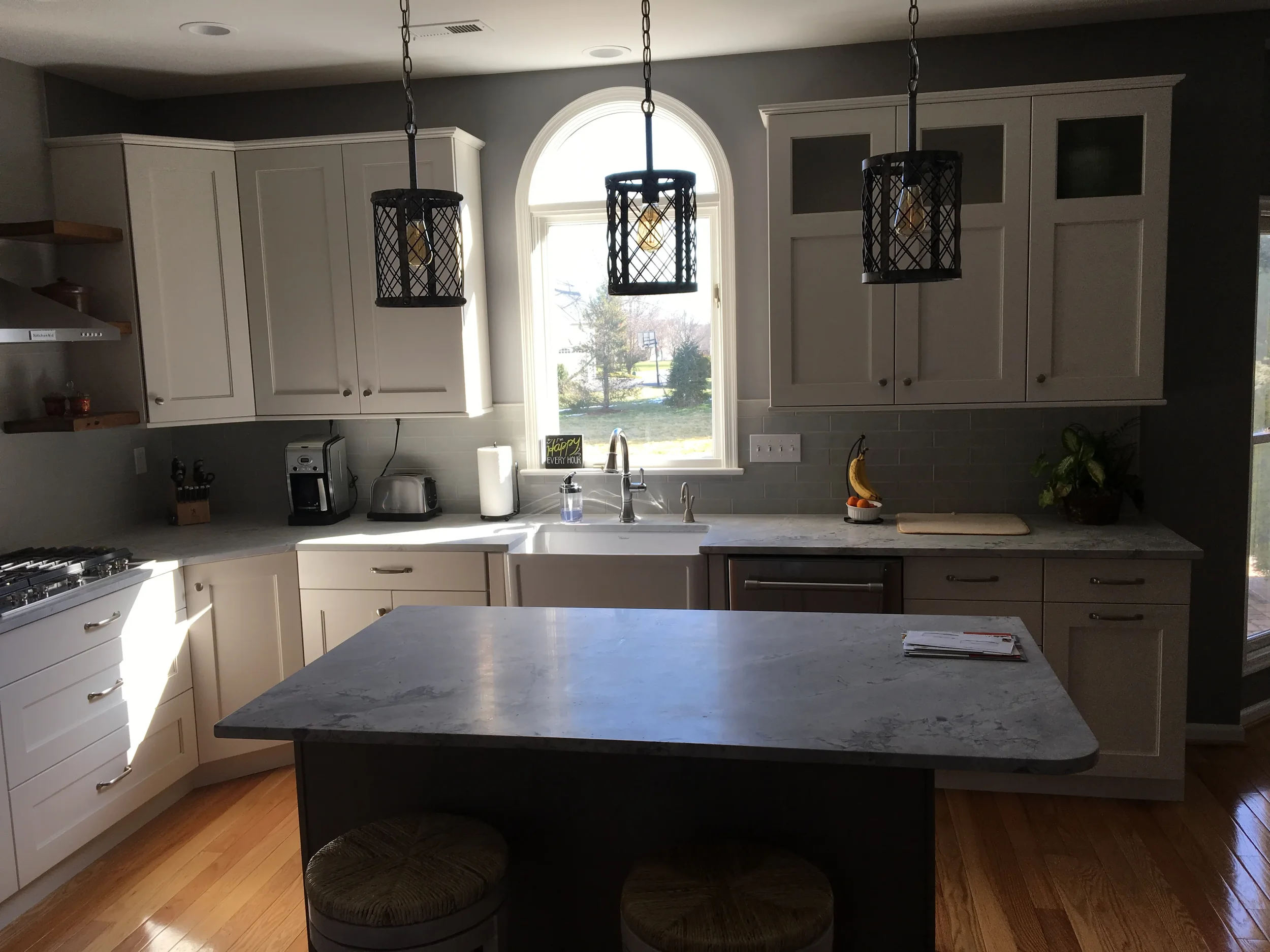 Kitchen with white cabinets, granite countertops, three pendant lights, a window above the sink, and wooden flooring.