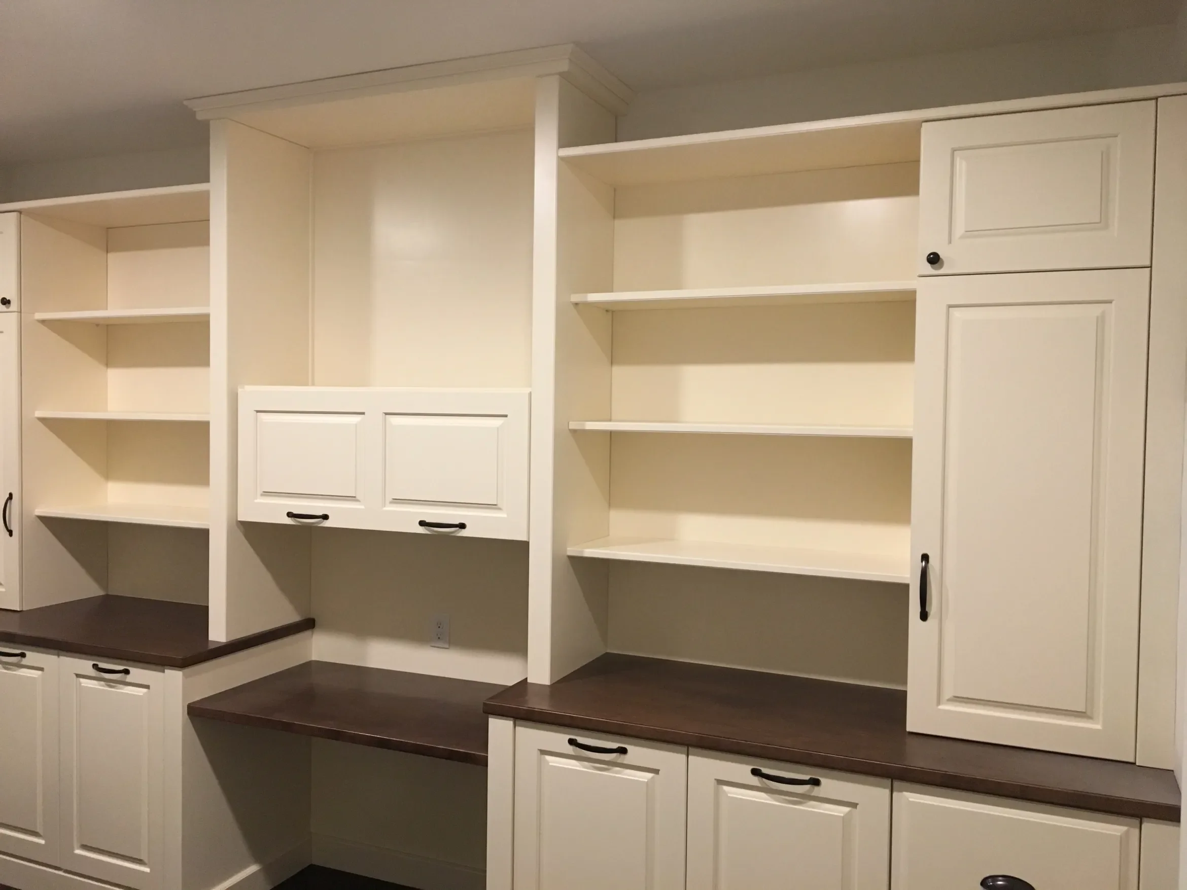 White built-in shelves and cabinets with dark brown countertops in a room.
