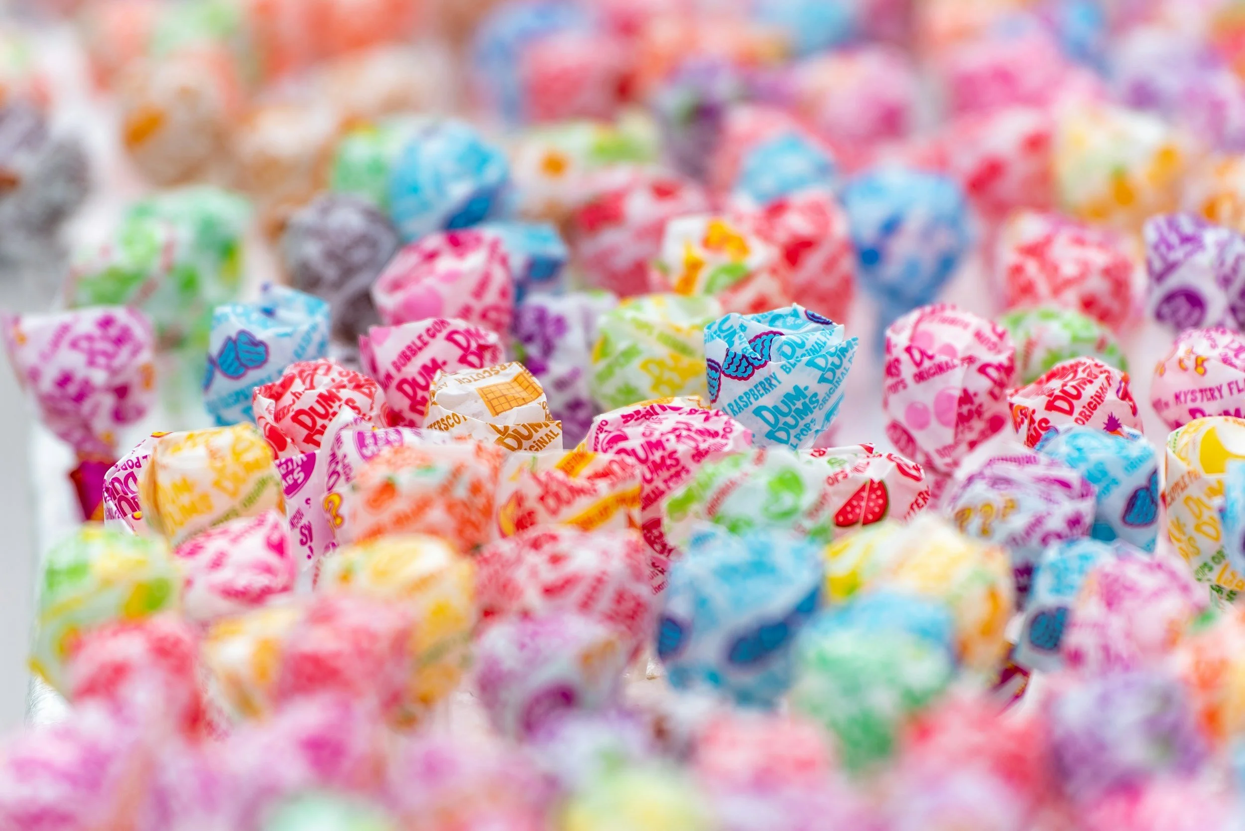 A colorful assortment of wrapped candies, including Dum Dums lollipops, in various bright colors.