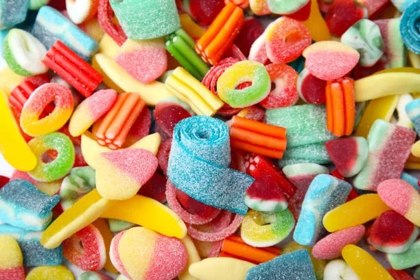 A colorful assortment of gummy candies including worms, bears, and fruit slices in various bright colors.