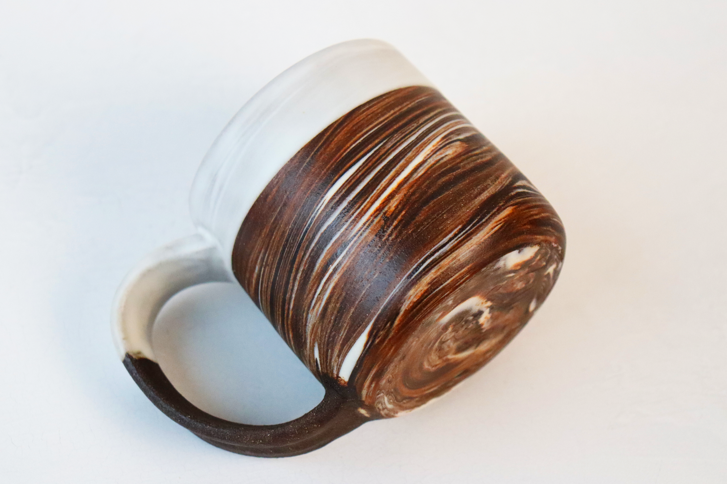 Dark brown stoneware and porcelain marbled mug with satin white glaze lying on its side