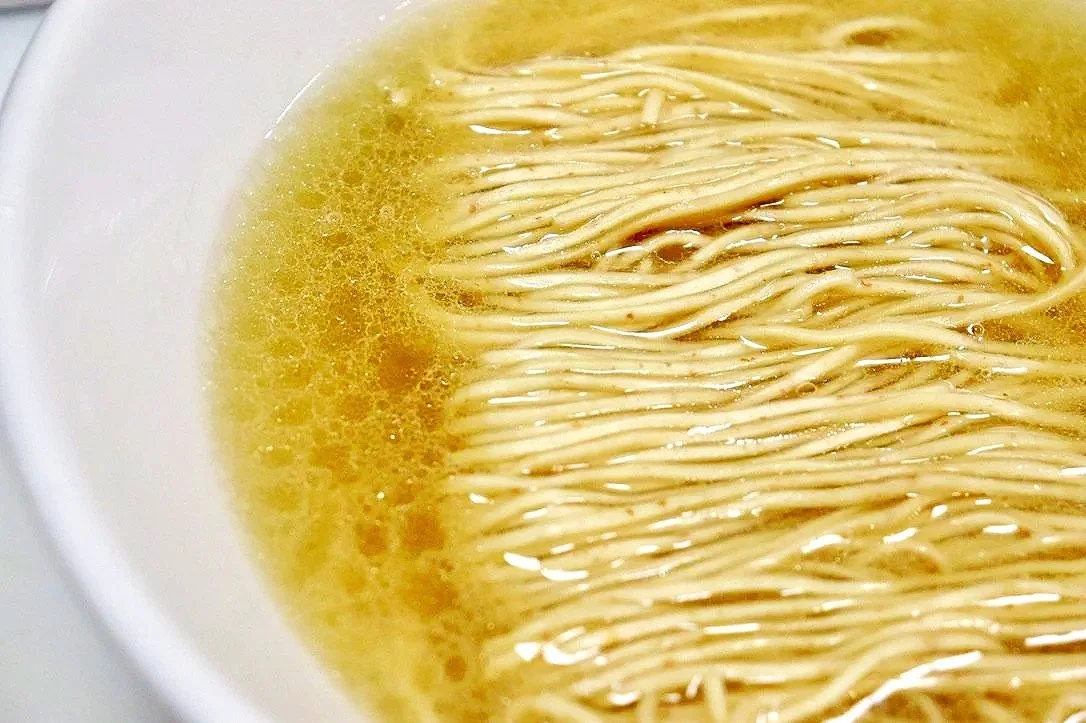Close-up of uncooked ramen noodles in hot chicken broth.