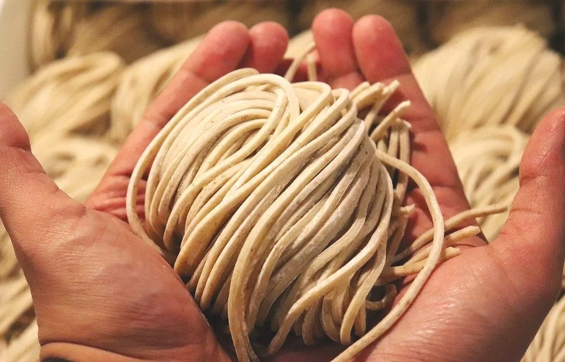 A person holding a bundle of handmade spaghetti noodles.