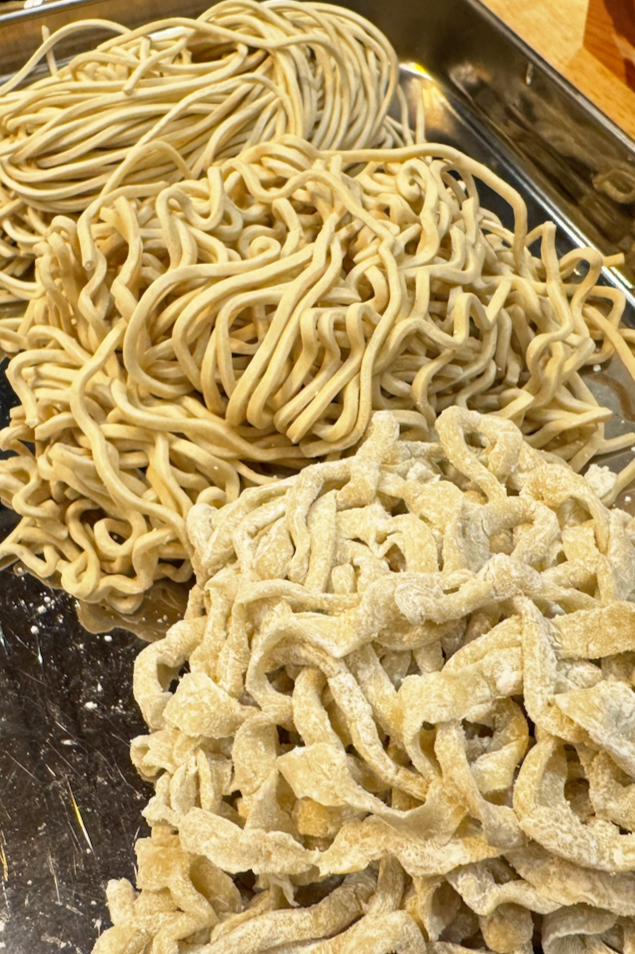Three different types of fresh, uncooked pasta on a metal tray.