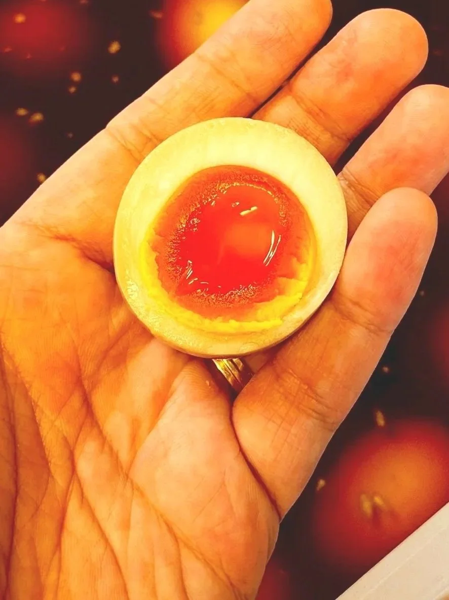 A hand holding a halved boiled egg with a soft yolk, with a blurred background of other eggs.