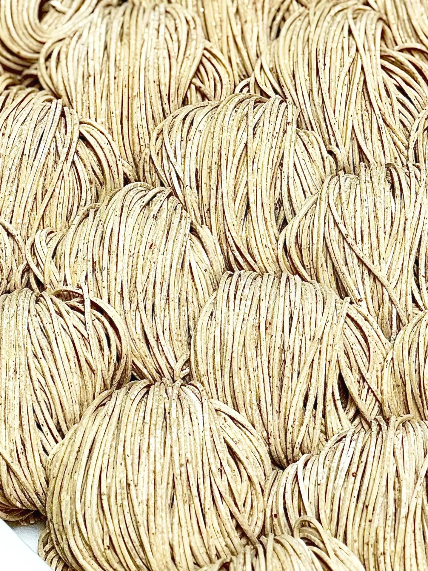 Close-up of several beige, crinkled, leaf-shaped edible objects with dark stripes, likely strands of dried pasta or noodles.