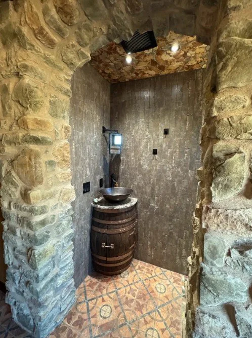 Small bathroom with stone and tile walls, a barrel-shaped sink with a bowl on top, and a wall-mounted telephone.