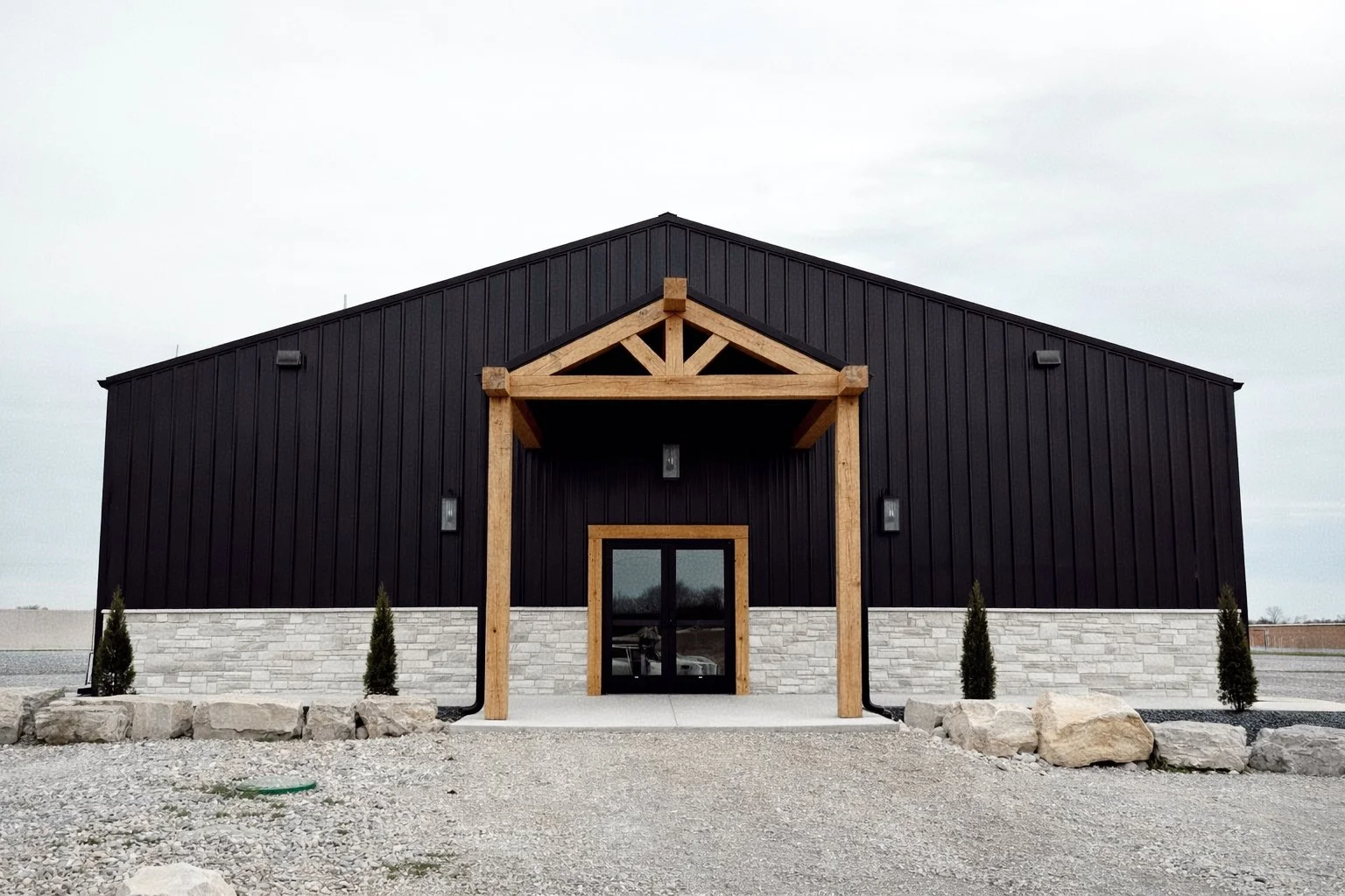 Front view of a modern black building with a wood porch and small trees in planters.