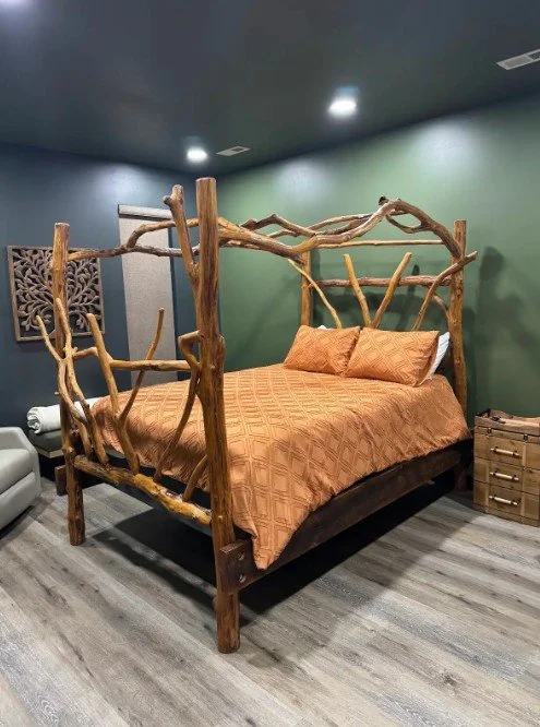 A bedroom with a rustic wooden bed frame made of intertwined branches, with an orange bedspread and pillows, green wall, wooden nightstand, and gray flooring.