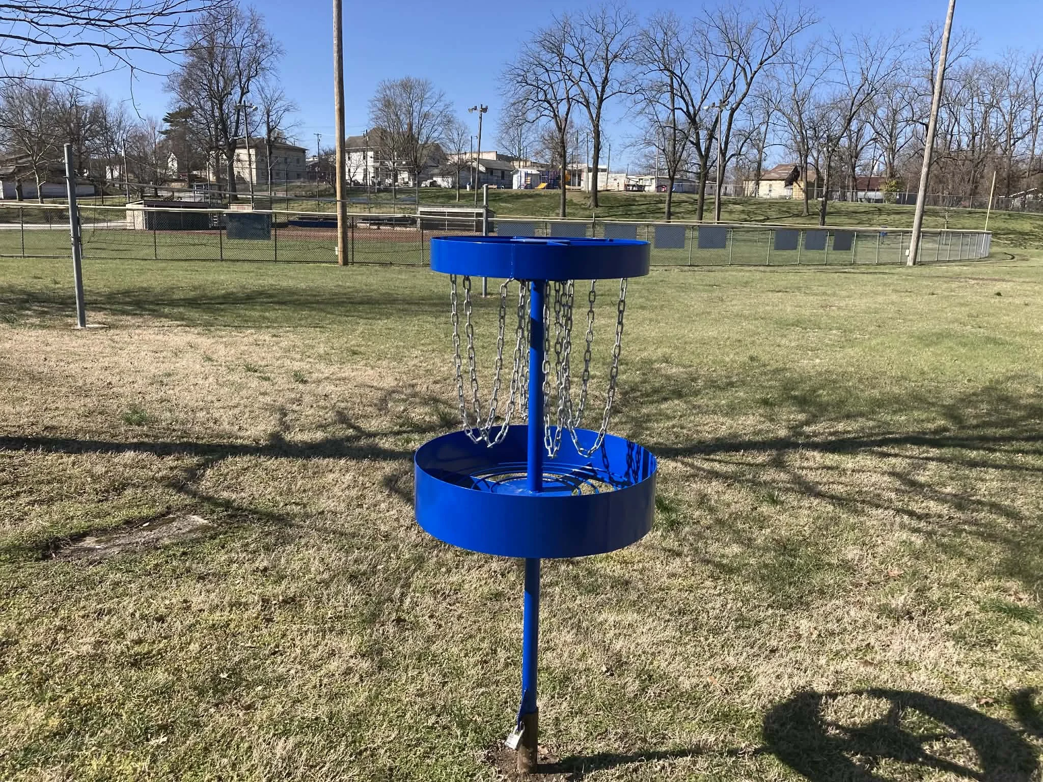 Blue disc golf basket in an open grassy field with trees and a fence in the background at Marionville, MO city park.