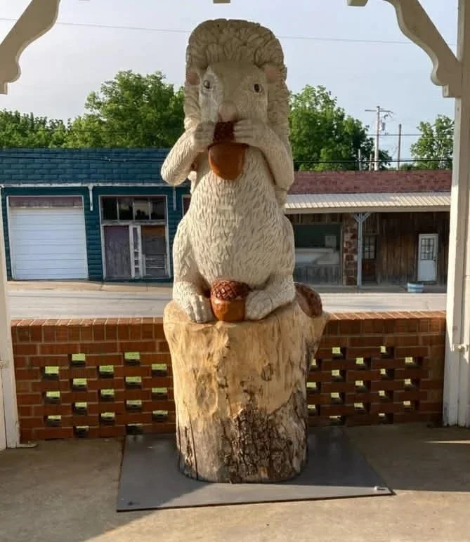 Carved wooden sculpture of a squirrel holding a nut, sitting on a tree stump porch