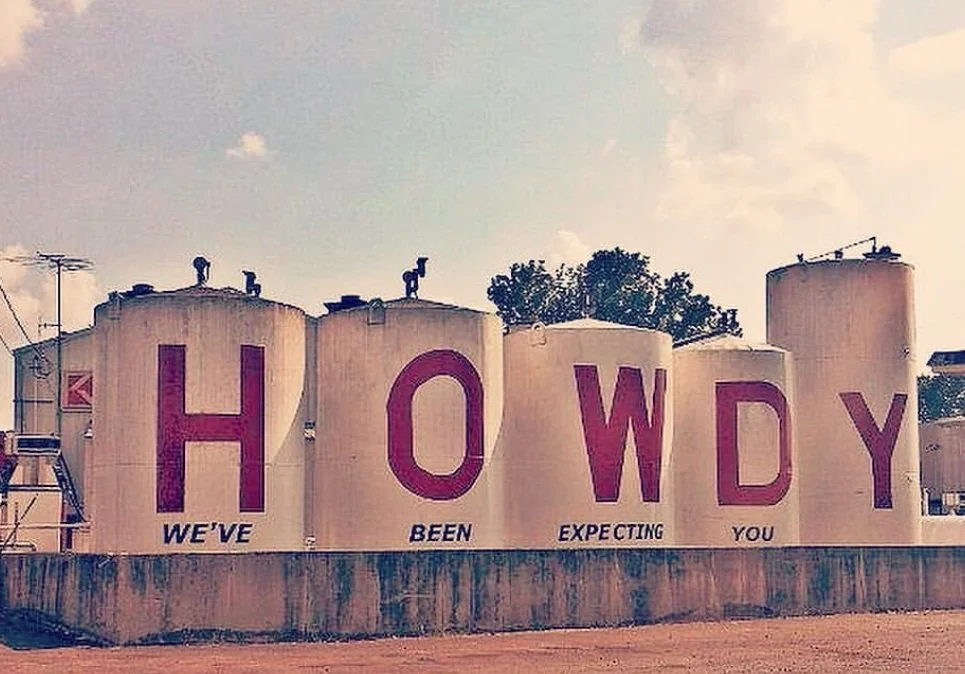 Large water tanks with red letters spelling "HOWDY" and smaller black text below saying "WE'VE BEEN EXPECTING YOU."