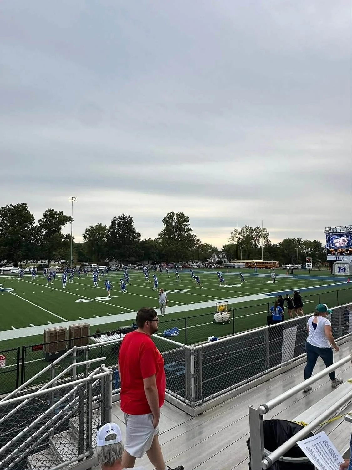 High school football game at a stadium with players on the field and spectators on the bleachers.