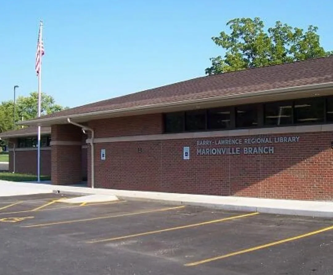 Brick public library building with sign reading 'Barry-Crawford Regional Library, Marionville Branch' and marked handicap parking spaces in front.