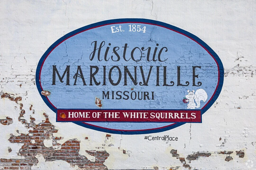 A mural on a brick wall welcoming visitors to Historic Marionville, Missouri, established in 1854, with a note about being home to white squirrels and a small cartoon squirrel holding an acorn.