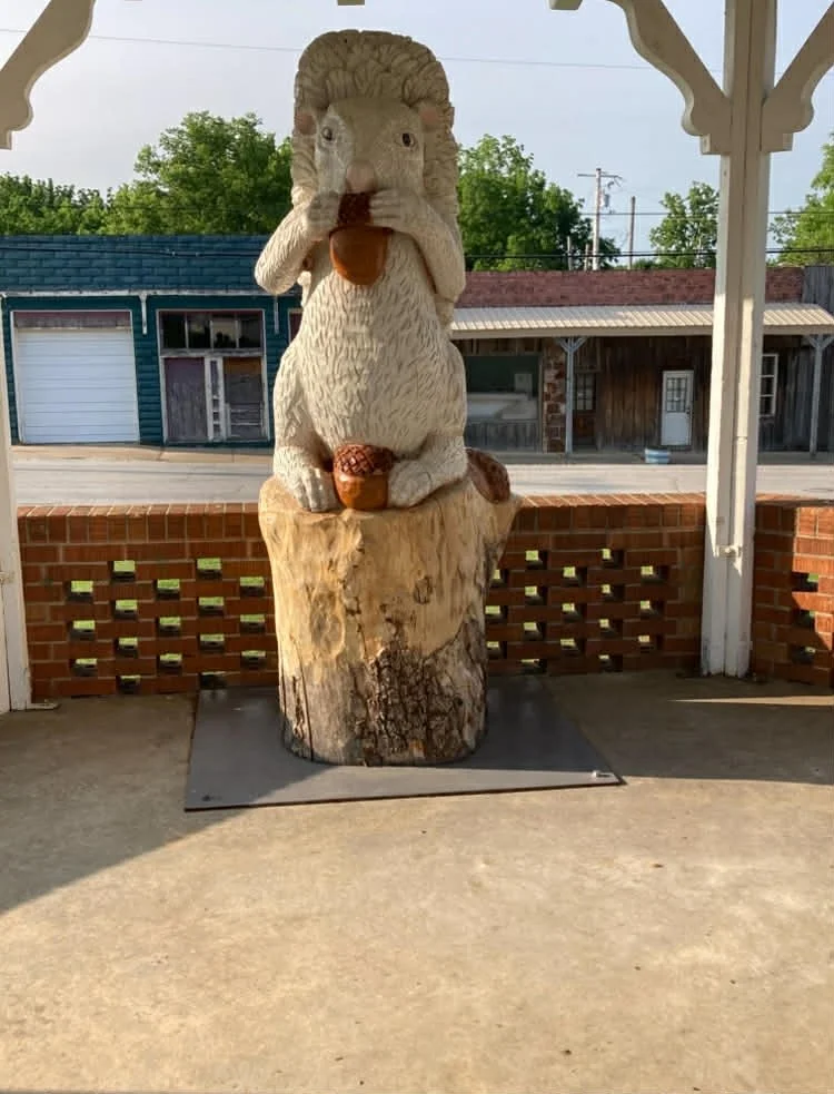 Wooden squirrel sculpture holding a nut, sitting on a tree stump on a porch.