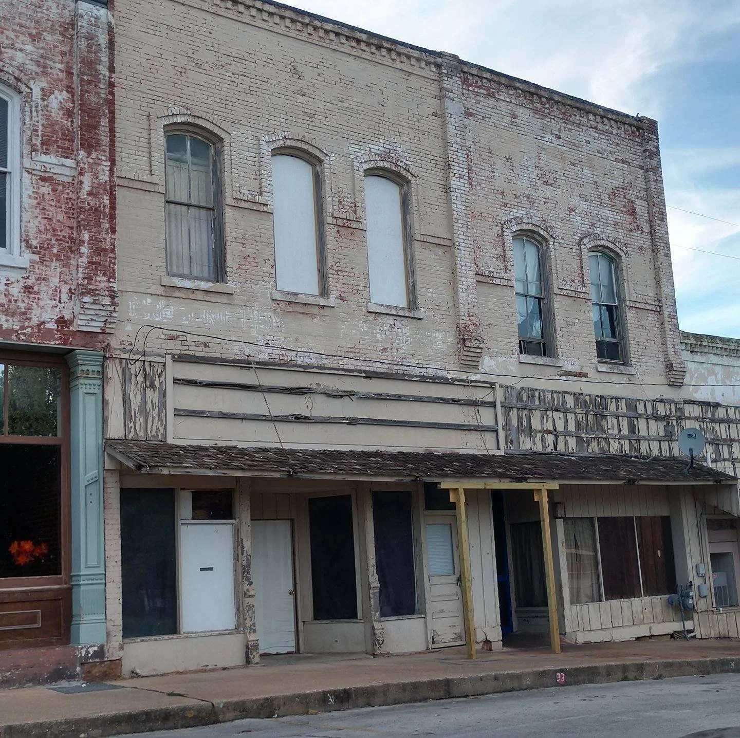 Old, weathered brick building with boarded-up and broken windows, and peeling paint on the exterior walls.