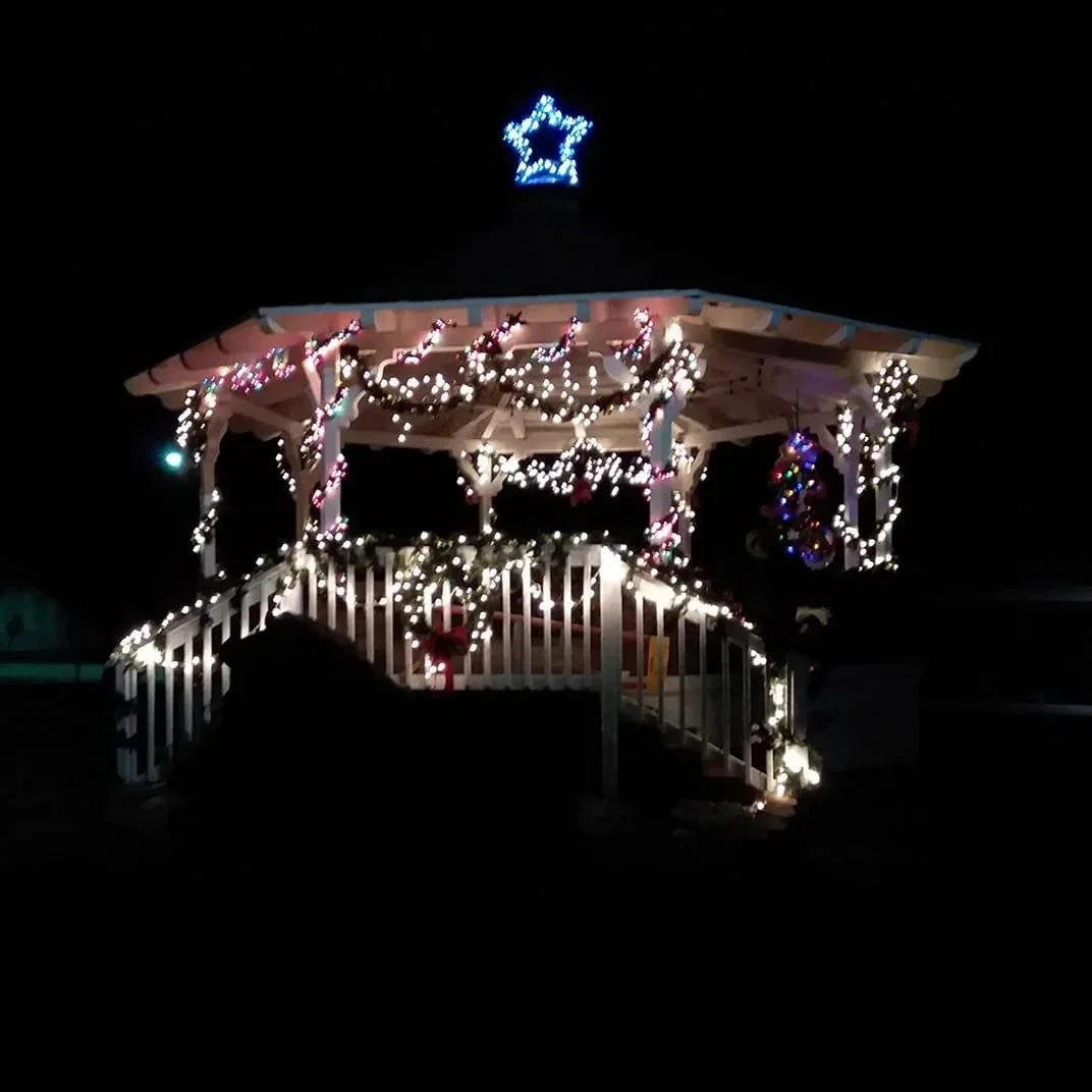 A decorated gazebo lit with string lights, garlands, and ornaments, topped with a star-shaped light on the roof, during nighttime.