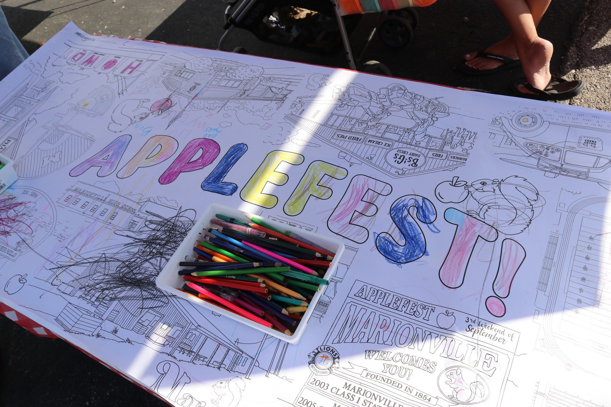 Colorful marker drawing sign on large paper at Applefest in Marionville, featuring the words "APPLEFEST!" in big, colorful letters with coloring supplies nearby.