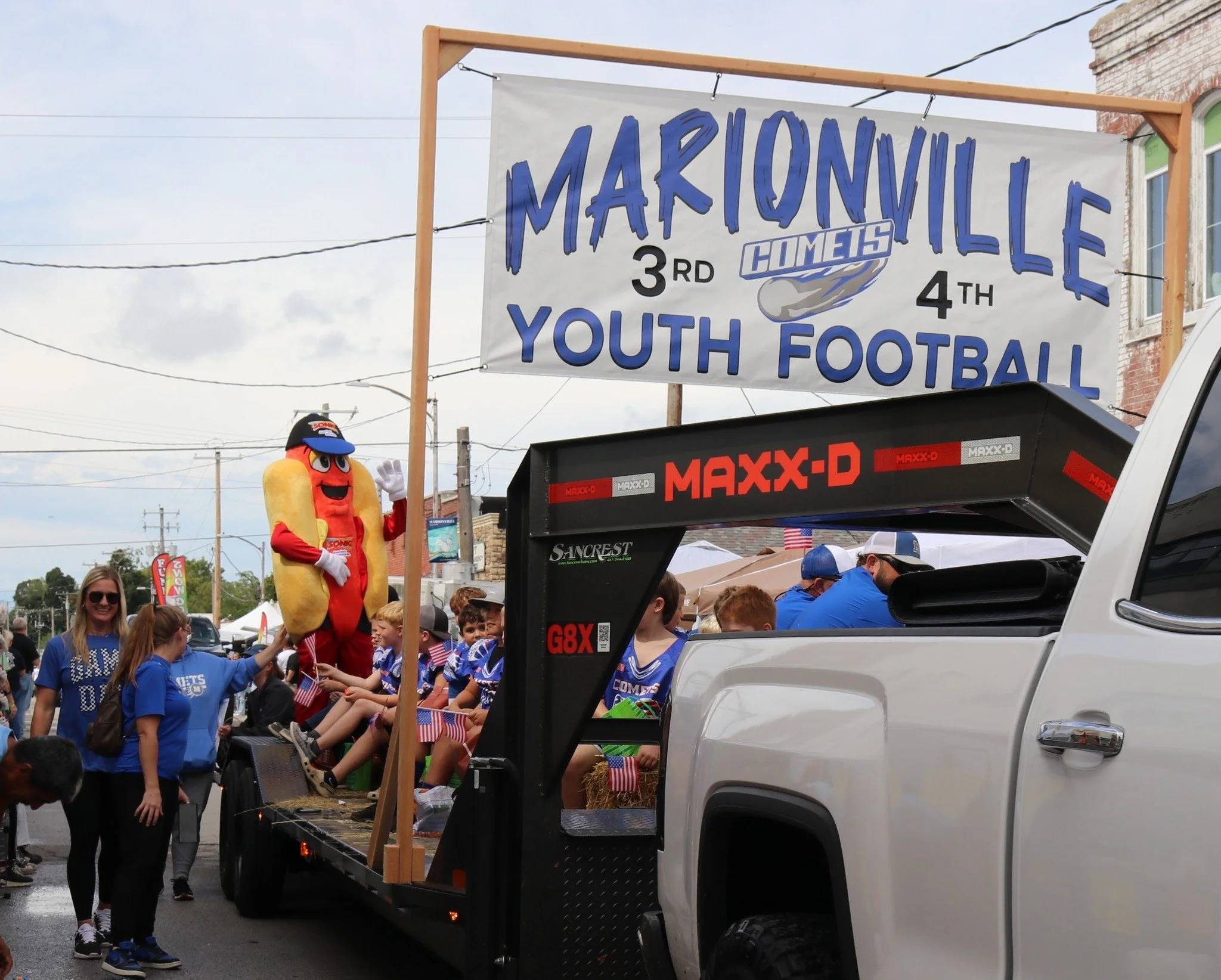 A parade float with children and adults, including a hot dog mascot, celebrating Marionville's 3rd and 4th Youth Football event.