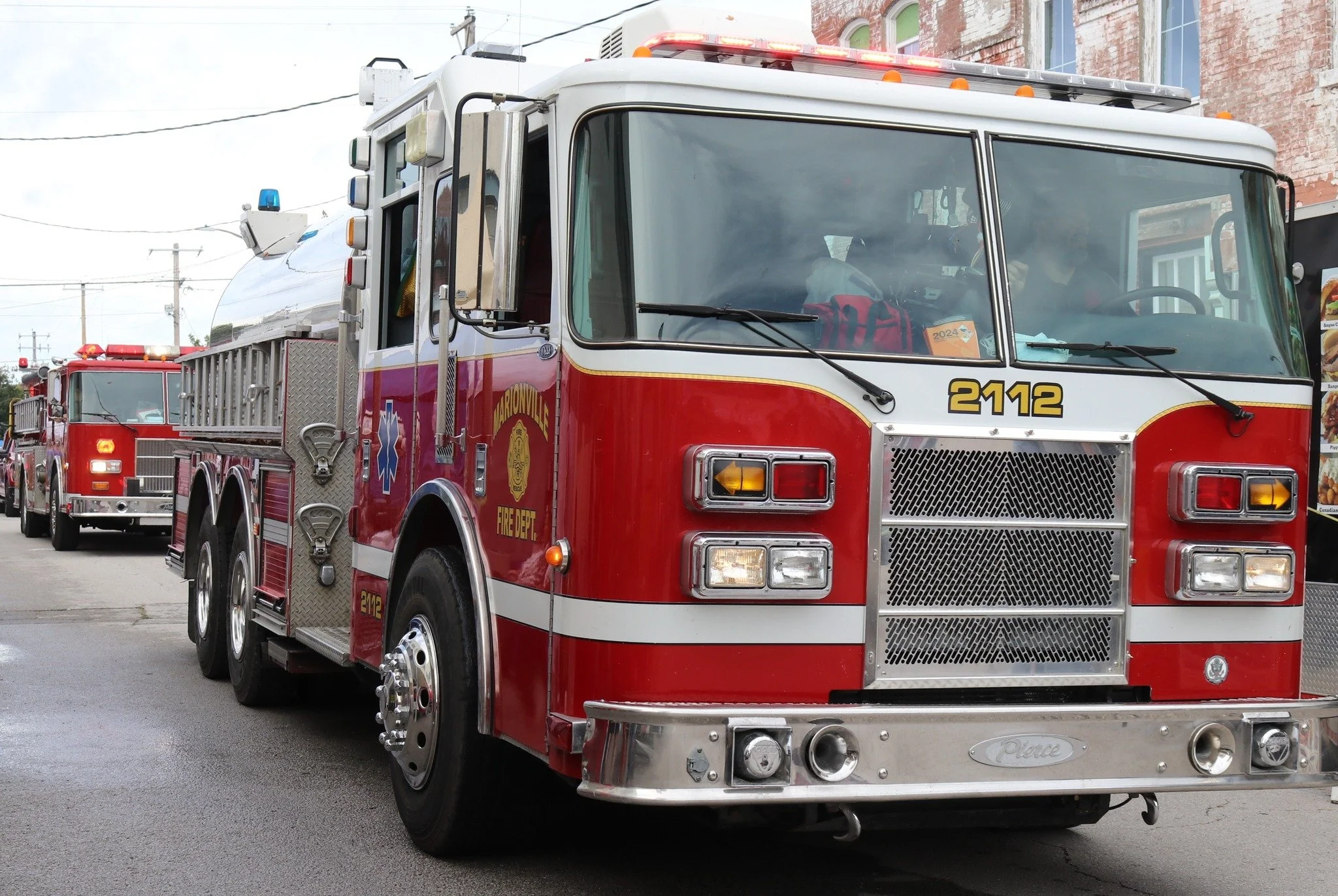 A red fire truck with the number 2112 parked on a city street, with another fire truck visible behind it.