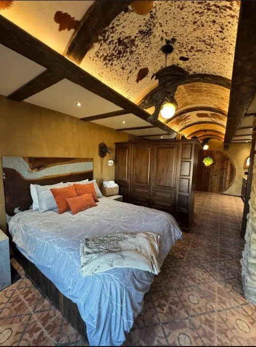 Bedroom with a bed, decorative pillows, a wooden wardrobe, and a curved ceiling with wooden beams and textured design.
