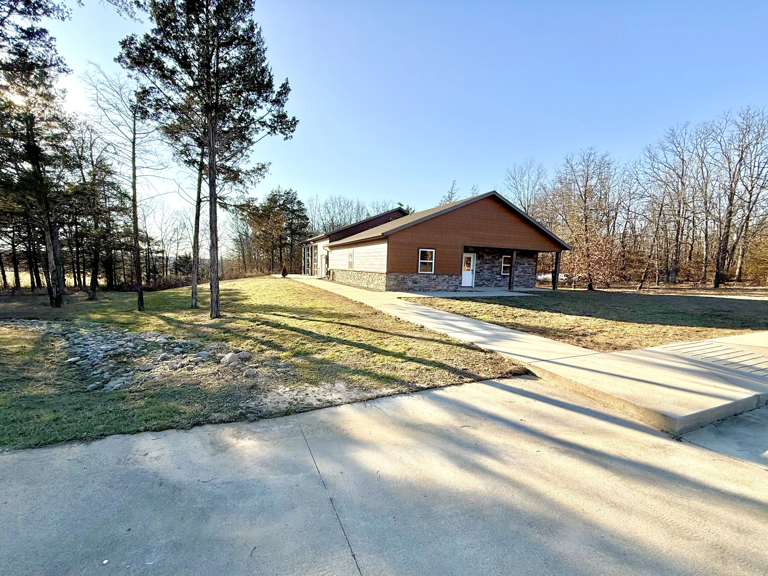 A modern house with a sloped roof, brick and wooden siding, surrounded by a lawn and trees, with a concrete driveway and walkway.