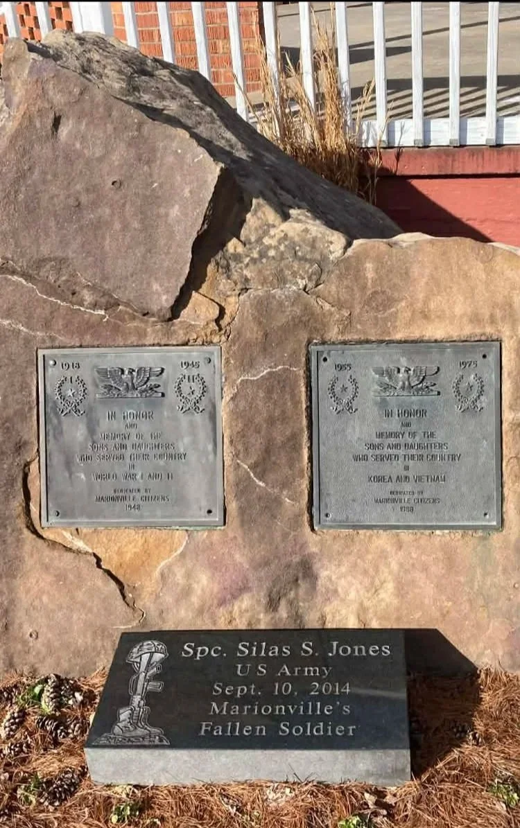 Three memorial plaques mounted on a rock with the Marionville gazebo in the background. The plaques honor soldiers who served in World War II, Korea, and Vietnam, including a fallen soldier from Marionville named Spc. Silas S. Jones