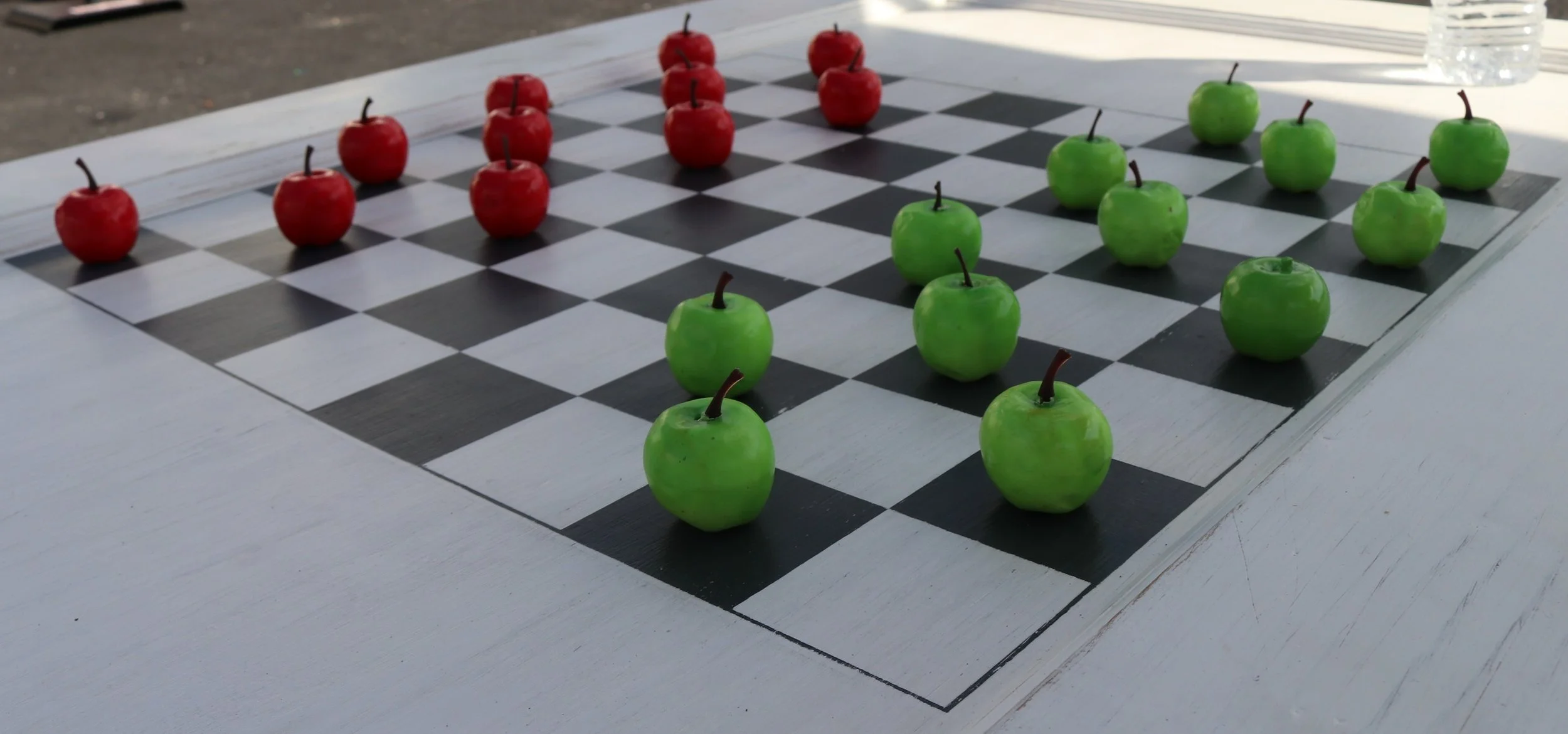 A chessboard with red apples on the black squares and green apples on the white squares, arranged to resemble a chess game.