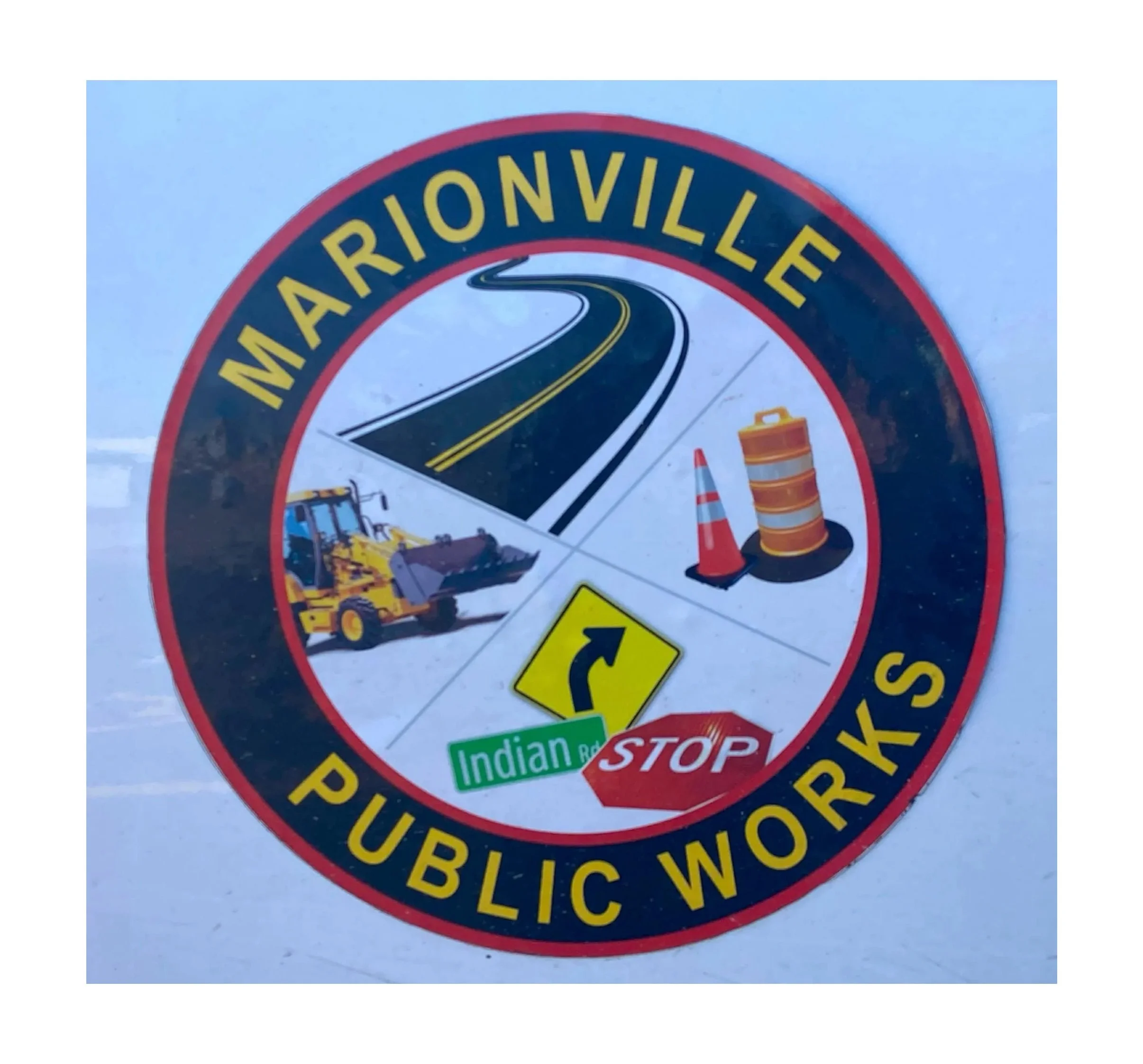 A circular sign with yellow text that reads 'Marionville Public Works' and pictures of a road, construction cones, a bulldozer, and a stop sign with an arrow and road name, indicating roadwork and road closure.